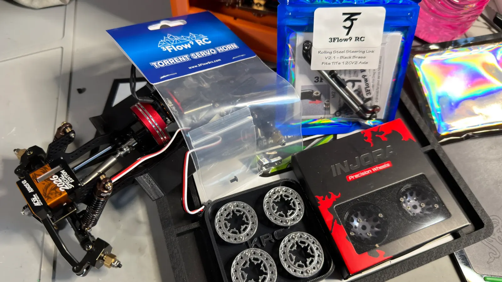 An assortment of SCX24 parts, a servo, wheels, and hardware on the bench